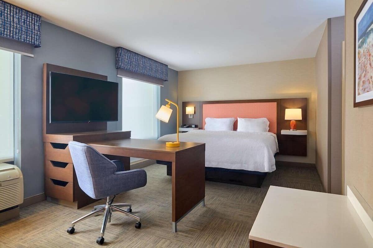 Quarto de hotel com cama, escrivaninha, cadeira, televisão e abajures.