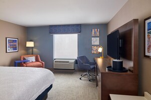 Habitación de hotel con cama, escritorio con computadora, silla, aire acondicionado y televisión.