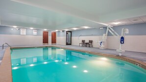 An indoor swimming pool with clear water, a changing room, and a lifeguard chair.