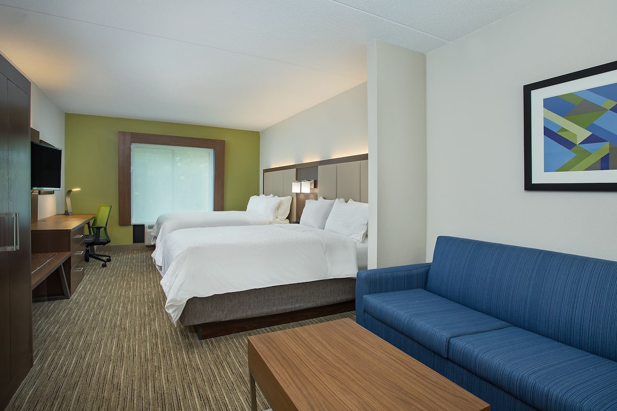 A hotel room with a bed, a blue sofa, a wooden coffee table, a desk with a chair, and a TV.