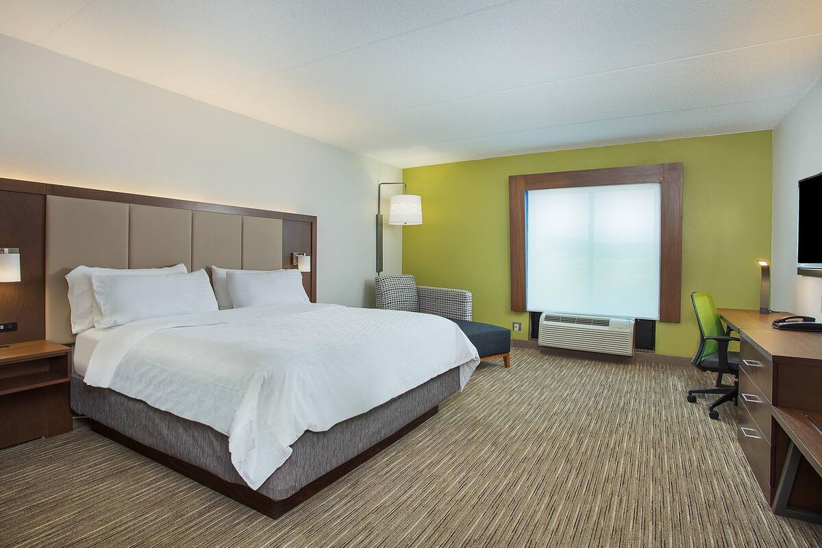 A hotel room with a large bed, a desk, a chair, a lamp, and a window.