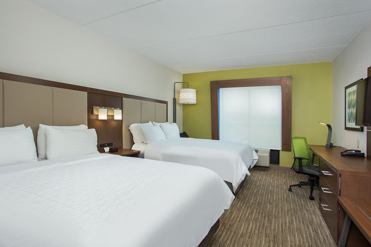 A hotel room with two beds, a desk, a chair, and a large window.