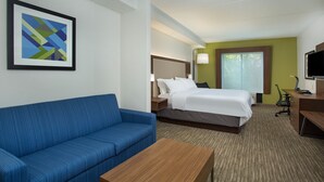 A hotel room with a blue sofa, a bed with white bedding, a desk with a computer, and a framed abstract artwork on the wall.
