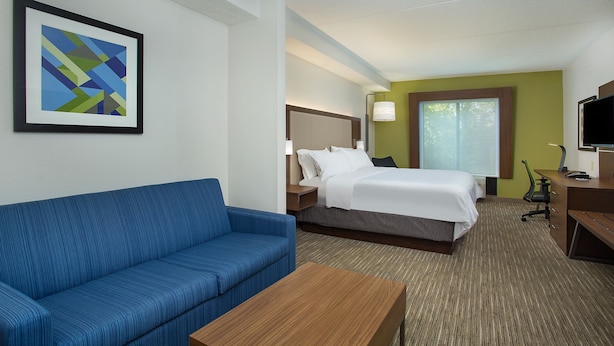 A hotel room with a blue sofa, a bed with white bedding, a desk with a computer, and a framed abstract artwork on the wall.