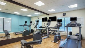 A gym with various exercise equipment, a large mirror, and a clock on the wall.