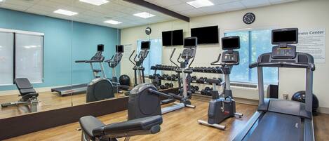 A gym with various exercise equipment, a large mirror, and a clock on the wall.