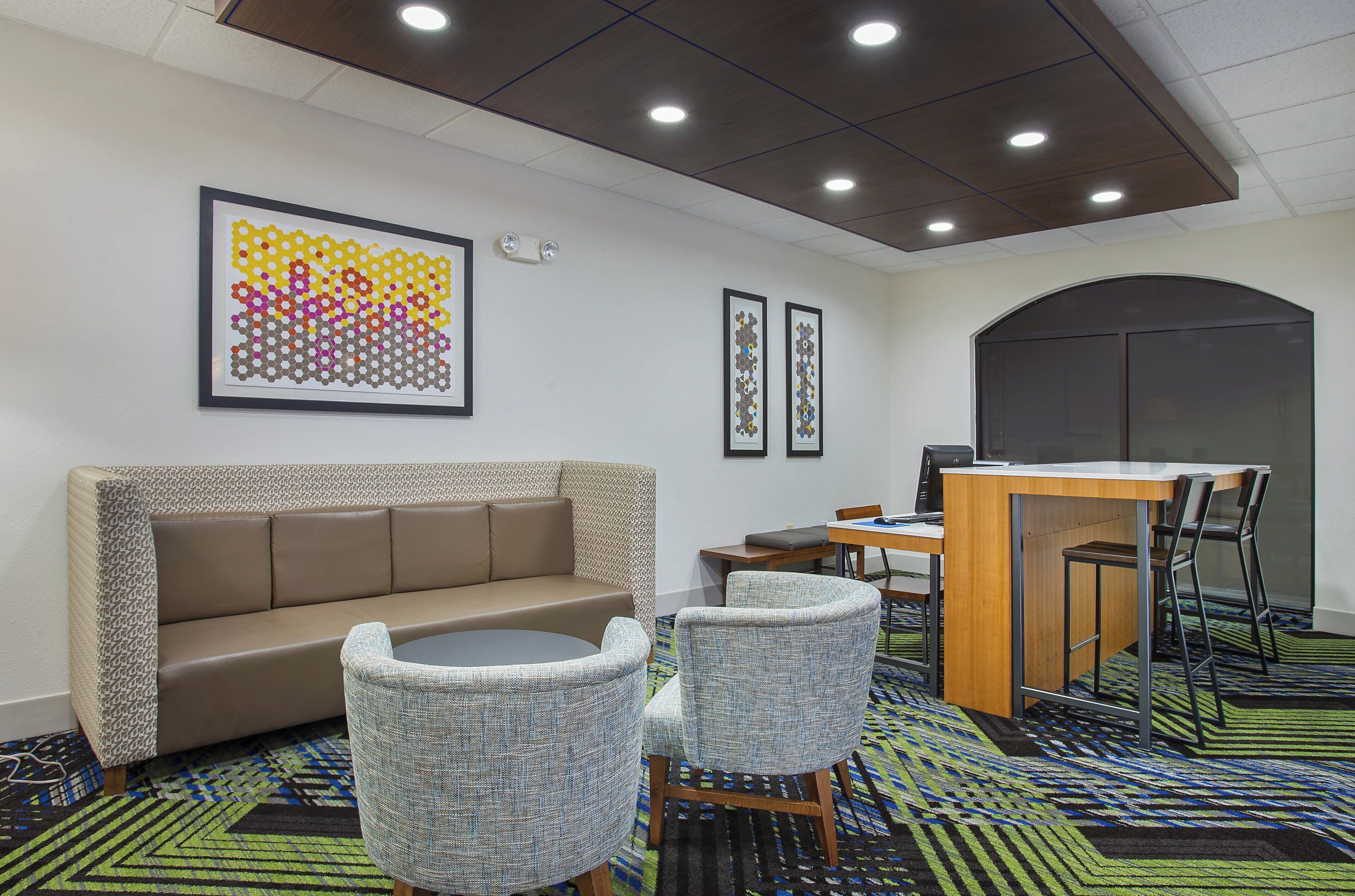A hotel room with a sofa, two chairs, a desk with a computer, and artwork on the wall.