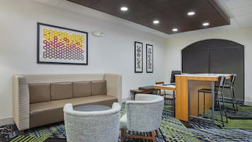 A hotel room with a sofa, two chairs, a desk with a computer, and artwork on the wall.