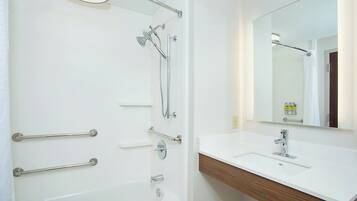 A modern bathroom with a bathtub, a shower, a vanity with a mirror, and handrails.