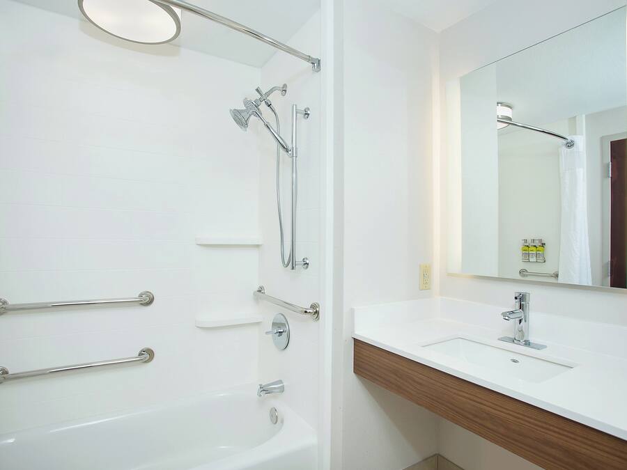 A modern bathroom with a bathtub, a shower, a vanity with a mirror, and handrails.