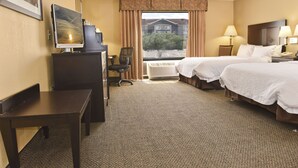A hotel room with two beds, a desk, a chair, a TV, and a window with a view of buildings and trees. - Hampton Inn & Suites Alexandria (Alexandria)
