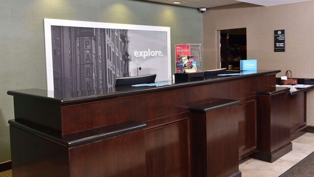 A reception desk with a large 'explore.' sign, a Hilton sign, and a 'Garage' sign in the background. - Hampton Inn & Suites Alexandria (Alexandria)