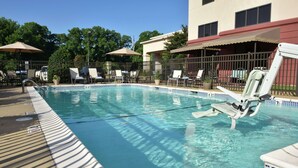 A clear swimming pool with lounge chairs and umbrellas, surrounded by a fence and trees. - Hampton Inn & Suites Alexandria (Alexandria)