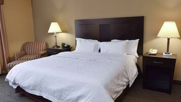 Ein Hotelzimmer mit einem großen Bett, zwei Nachttischen mit Lampen, einem Sessel und einem kleinen Tisch mit Telefon.
