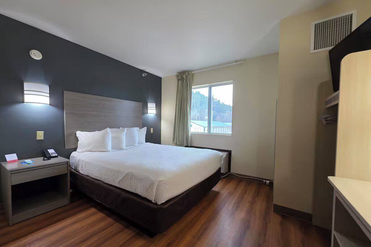 A hotel room with a large bed, bedside table, a window with a view, and a built-in heater.