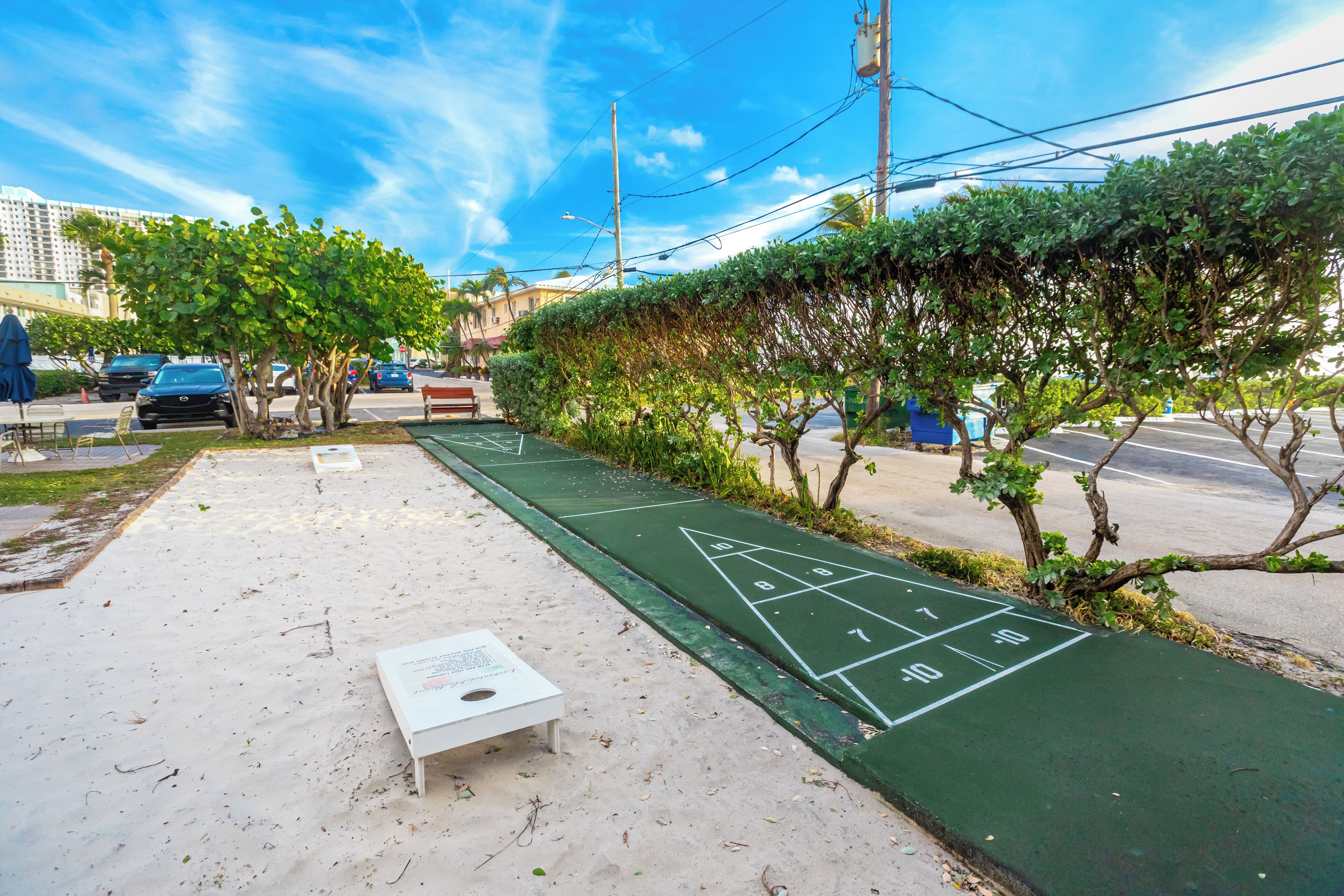 A green shuffleboard court with a white table in the foreground, surrounded by trees and a sidewalk.