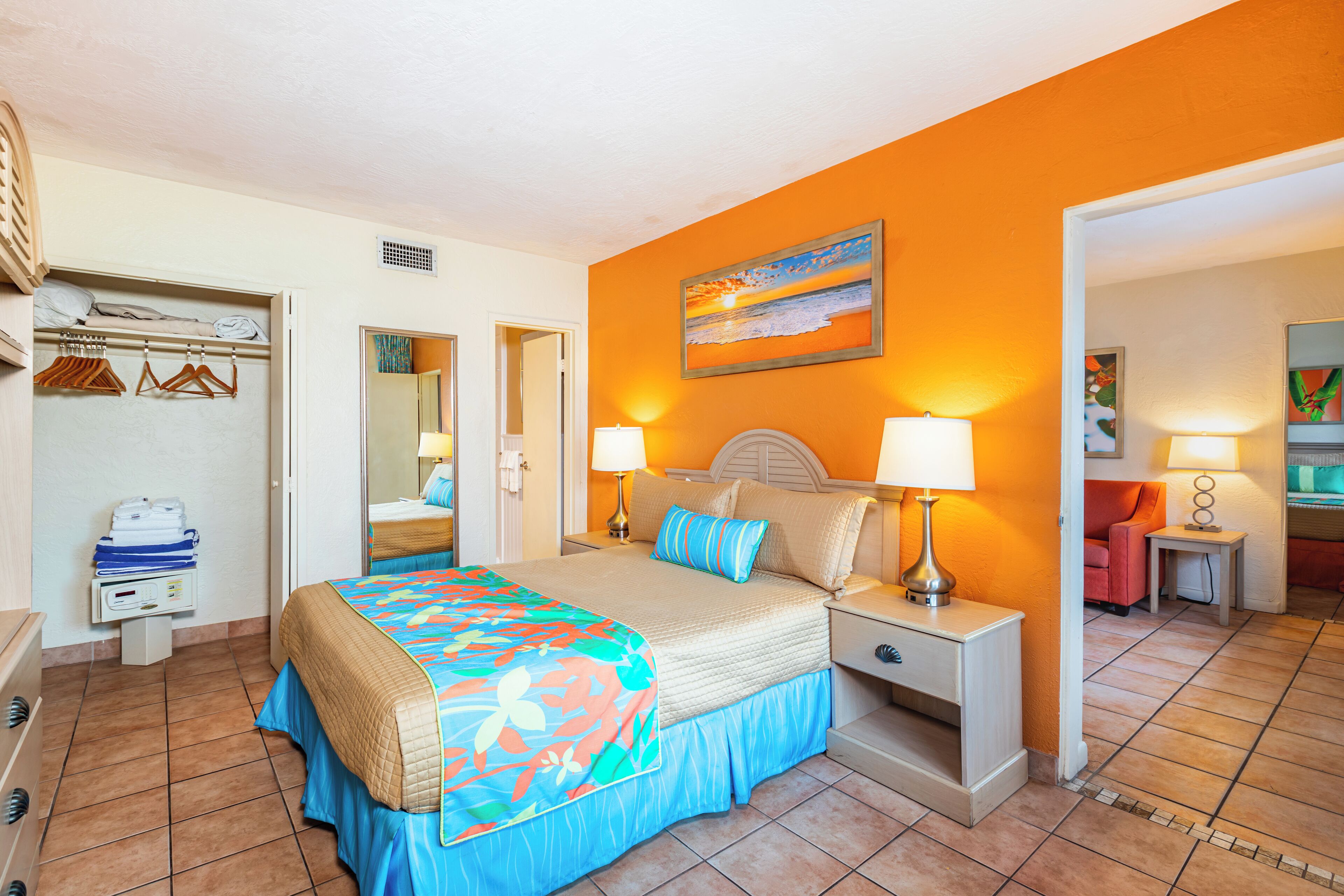 A bedroom with a bed, bedside lamps, a nightstand, a dresser, and a closet with hanging clothes.