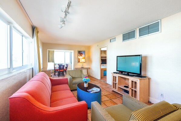 A living room with a red sofa, a patterned armchair, a blue coffee table, and a television on a wooden stand.