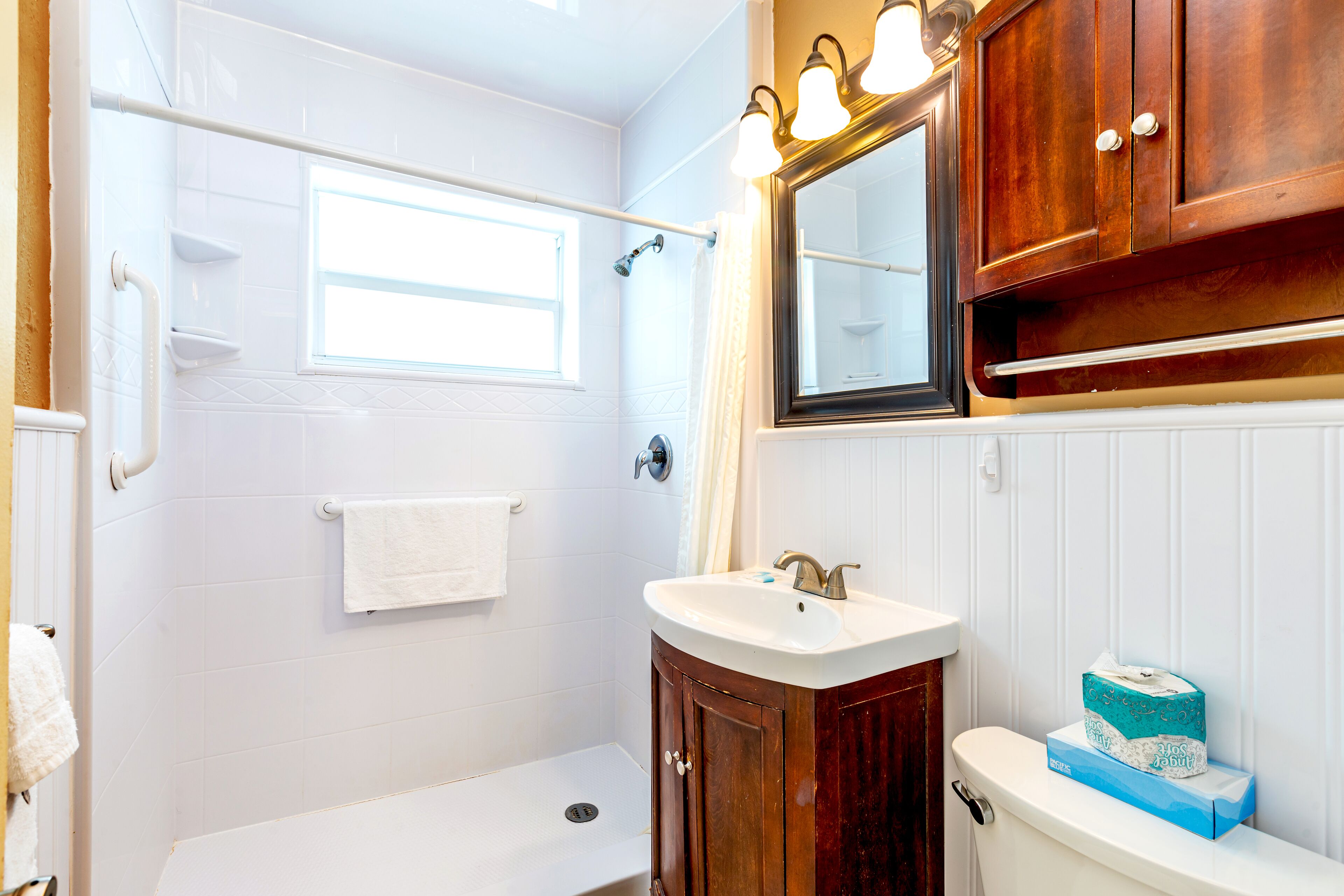 A bathroom with a white bathtub, a wooden vanity with a sink, a mirror, and a towel rack.