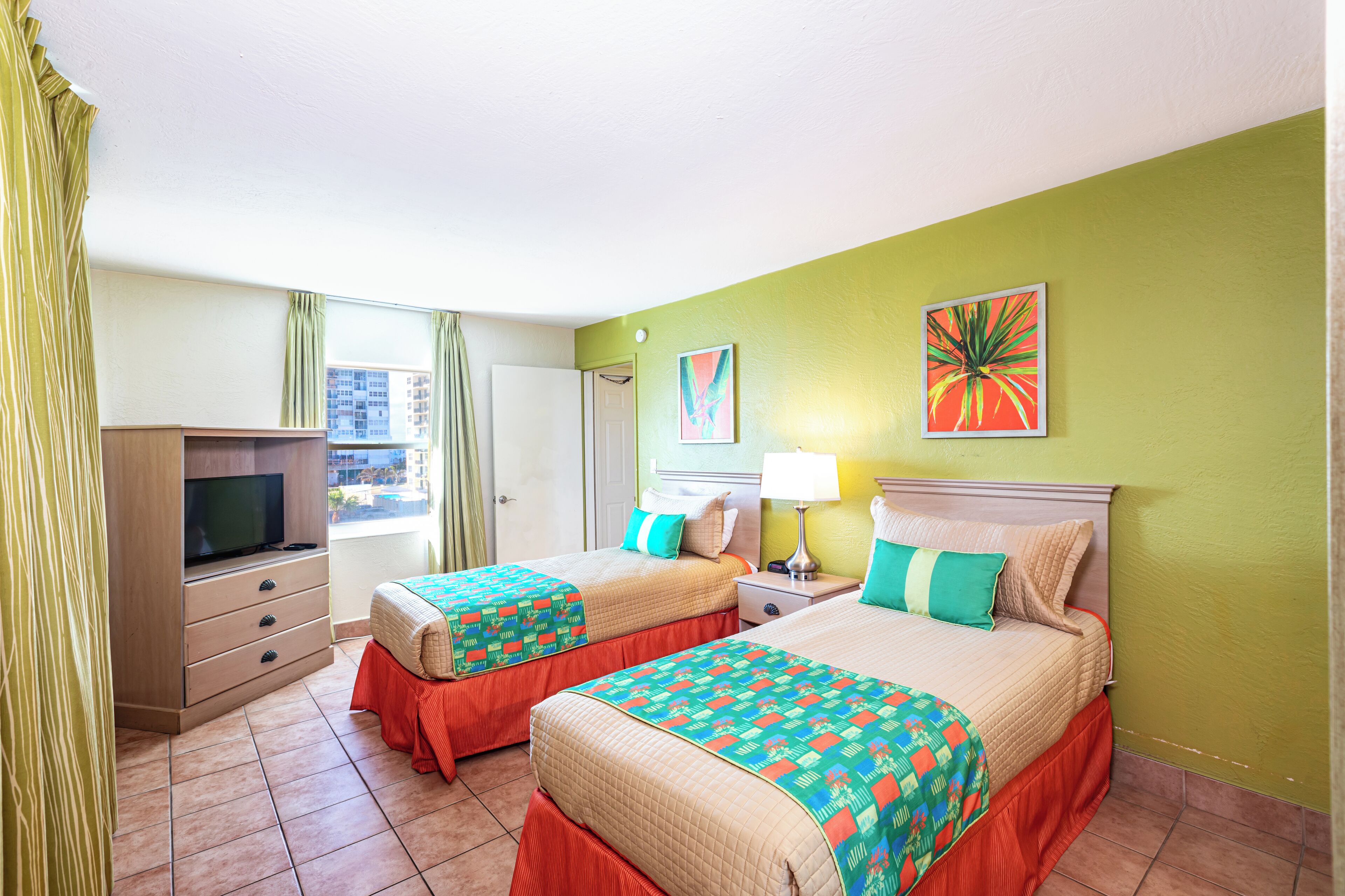 Une chambre d’hôtel avec deux lits, une télévision, un bureau et une fenêtre avec des rideaux.