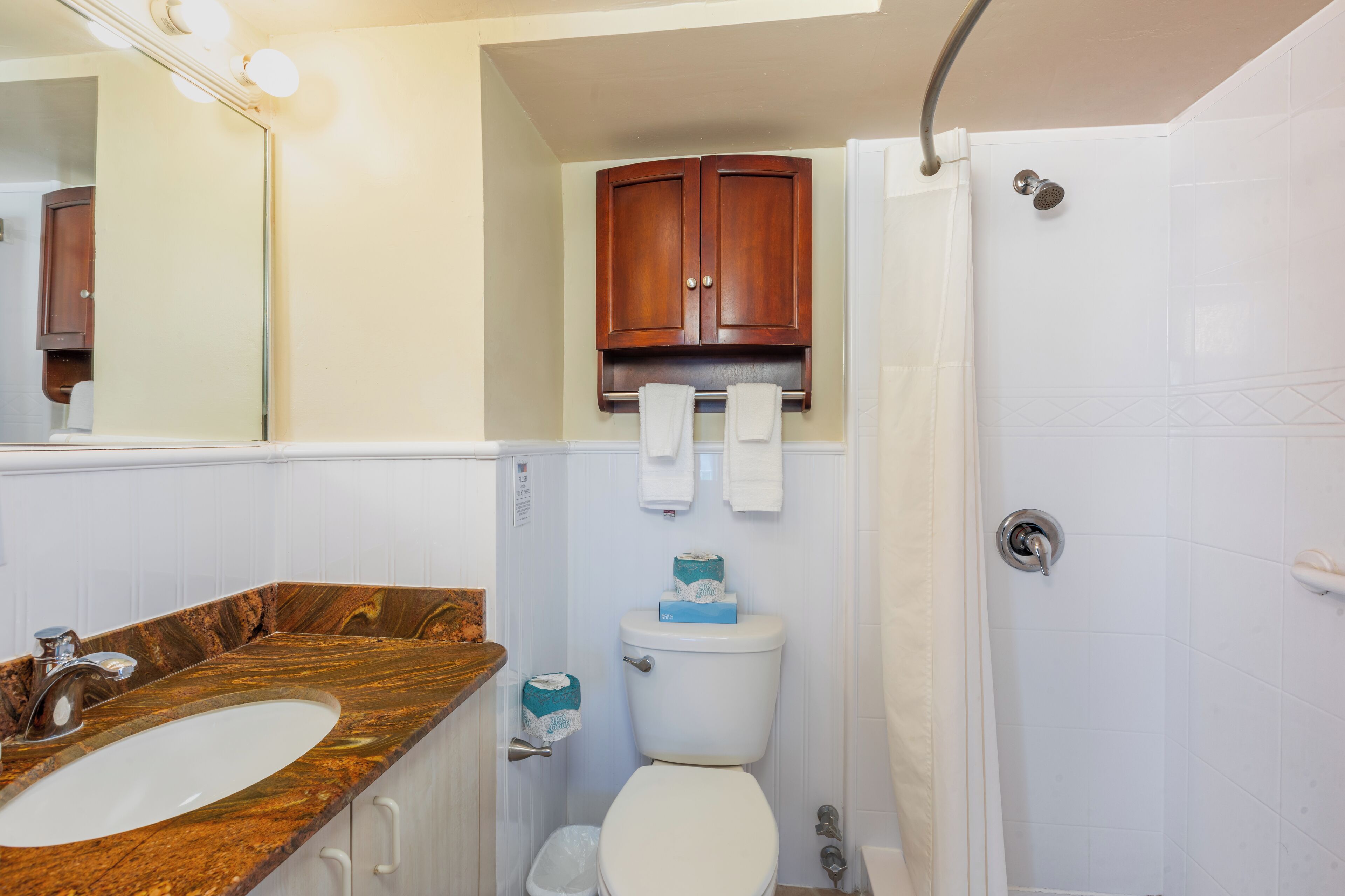 Une salle de bain avec un lavabo en marbre, des toilettes, une douche et un meuble en bois au-dessus des toilettes.