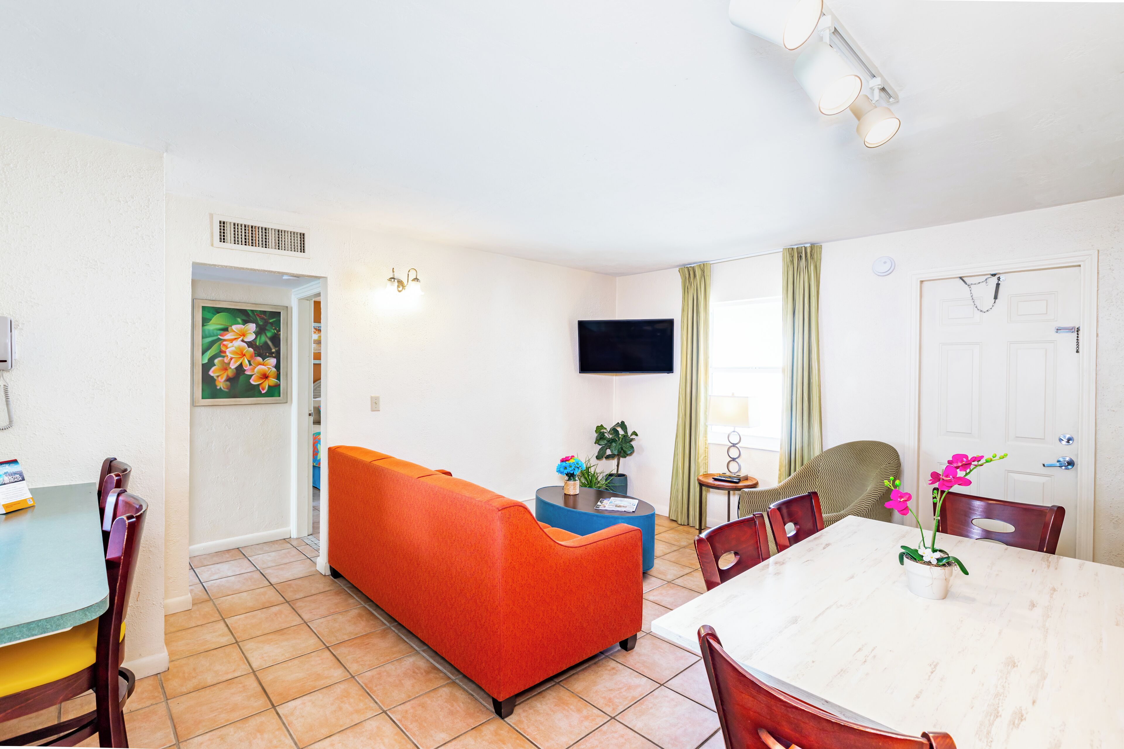 A compact living space with a dining area, a sofa, a TV, and a door with a chain.