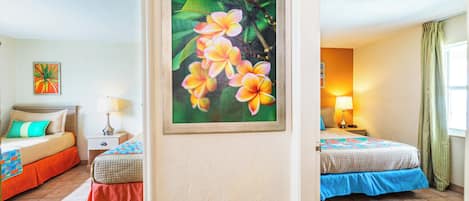 A hotel room with two beds, a nightstand, a lamp, a painting of flowers, and a window with curtains.