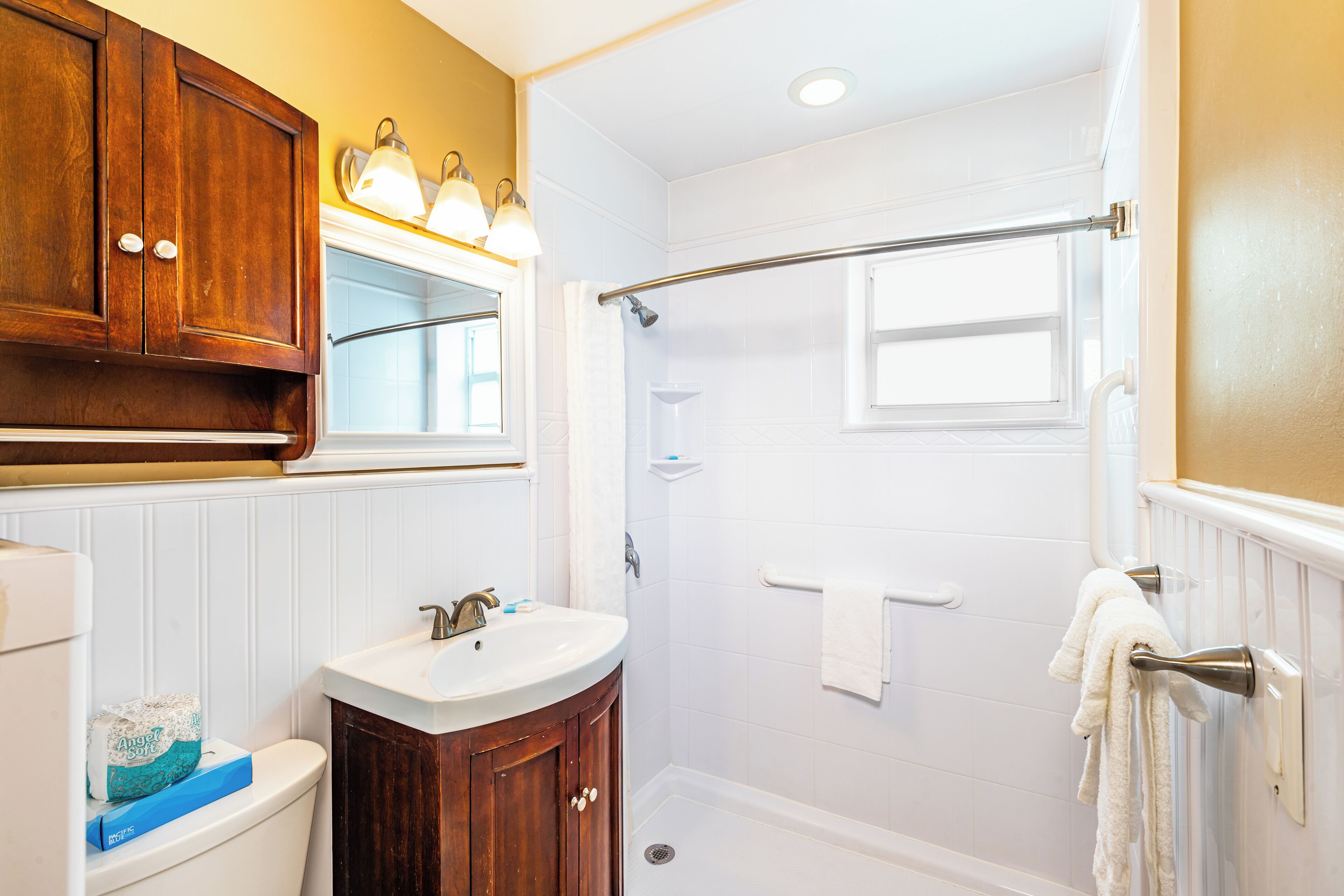 Une salle de bain avec un lavabo blanc, un meuble-lavabo en bois et une douche à l’italienne.