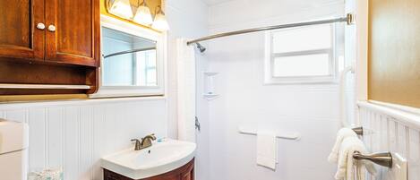 Une salle de bain avec un lavabo blanc, un meuble-lavabo en bois et une douche à l’italienne.