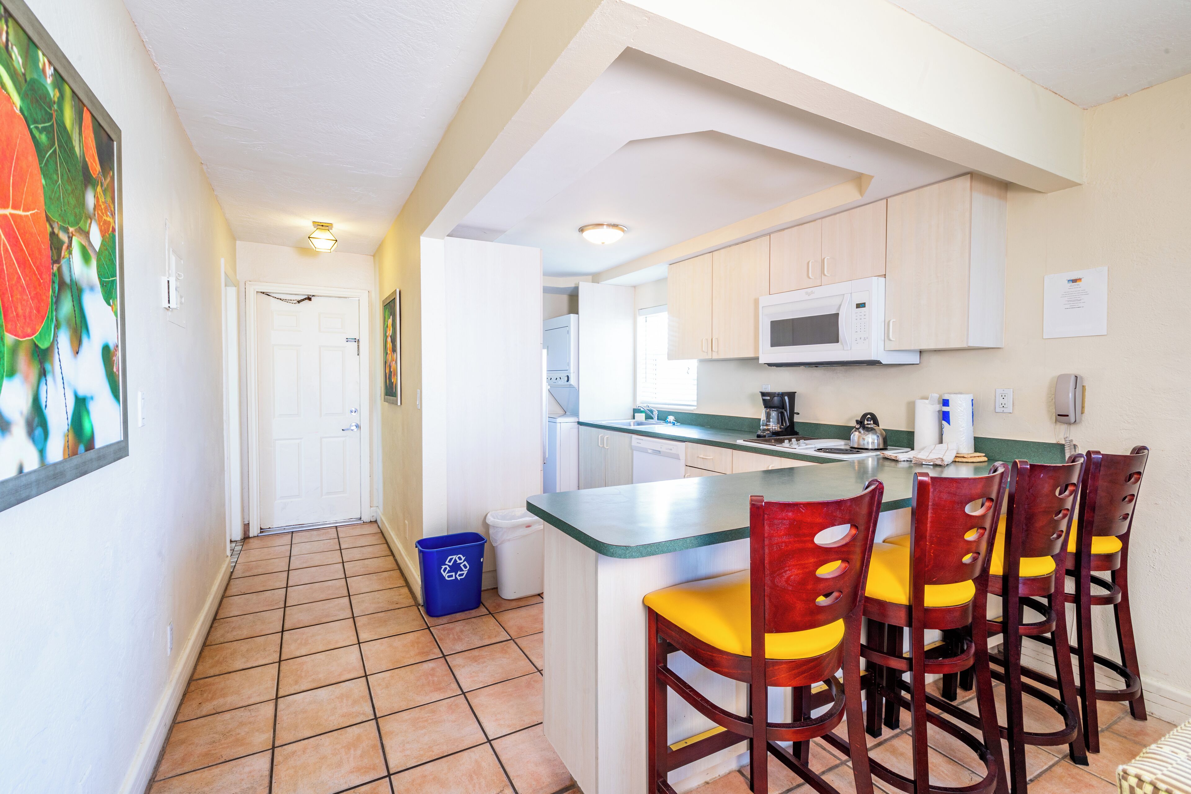A kitchen with a central island, wooden chairs, a microwave, and a trash bin.