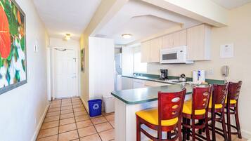 A kitchen with a central island, wooden chairs, a microwave, and a trash bin.