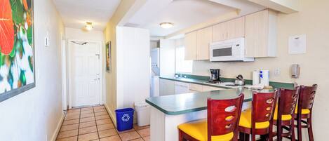 A kitchen with a central island, wooden chairs, a microwave, and a trash bin.