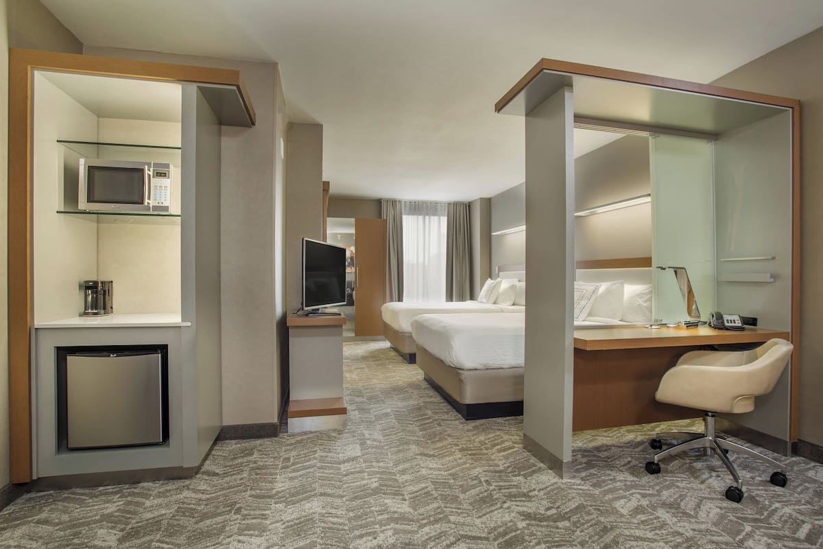Ein Hotelzimmer mit einem Bett, einem Schreibtisch mit Stuhl, einem Fernseher, einer Mikrowelle und einem kleinen Kühlschrank.