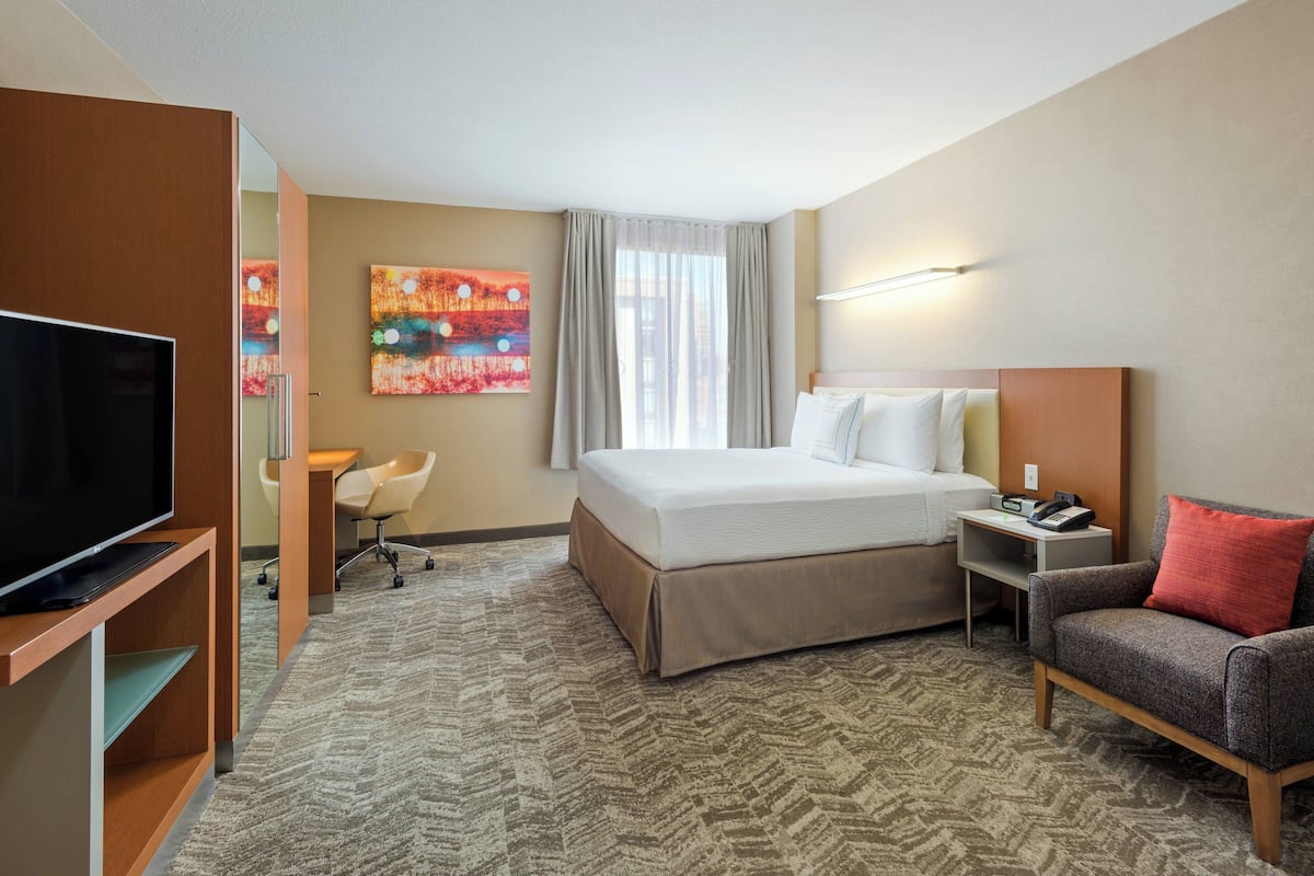 Ein Hotelzimmer mit Bett, Fernseher, Schreibtisch, Sessel und einer Couch.