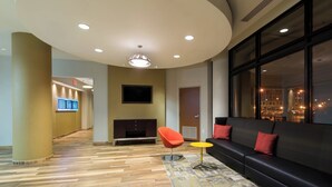 Un hall d’entrée moderne avec un plafond incurvé, un canapé noir agrémenté de coussins rouges, un fauteuil rouge et une petite table jaune.
