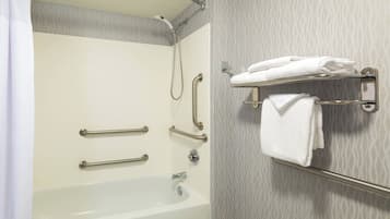 A bathroom with a bathtub, grab bars, a towel rack, and a shower head.