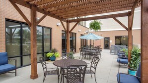 Un espace extérieur aménagé en terrasse, avec une pergola en bois, des tables, des chaises et des plantes en pot.