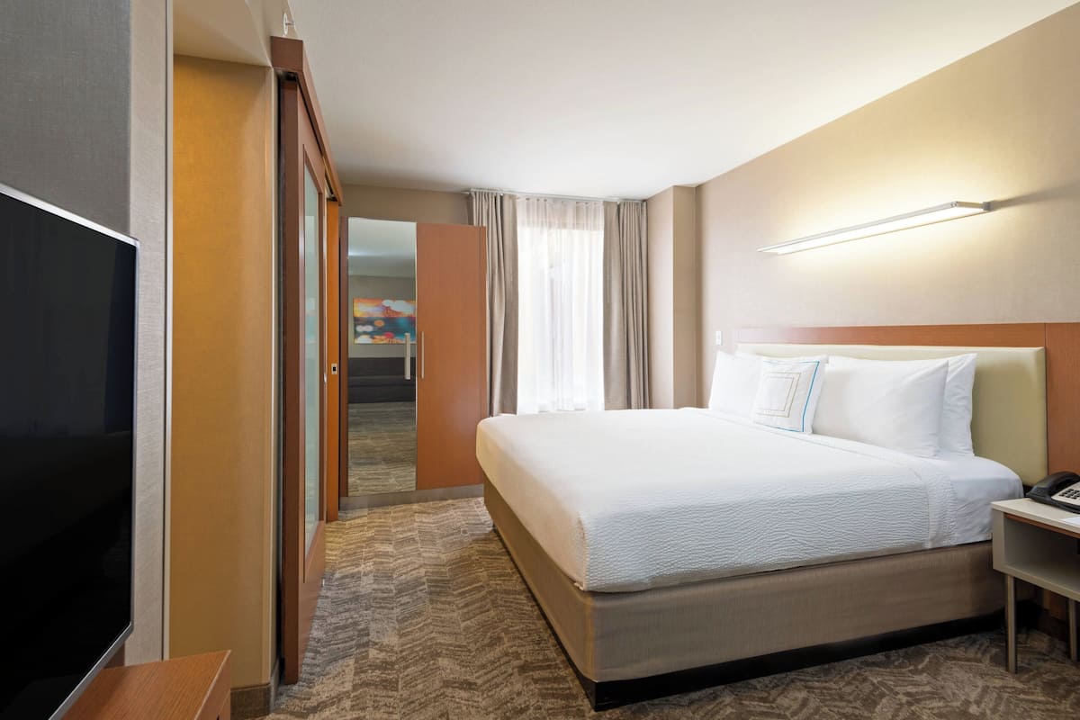 Ein Hotelzimmer mit einem großen Bett, einem Flachbildfernseher, einem Nachttisch und einer Tür zu einem Flur.