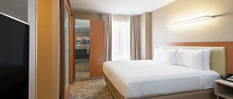 A hotel room with a large bed, a flat-screen TV, a bedside table, and a door leading to a hallway.