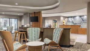A hotel lobby with wooden chairs, a reception desk, a flat-screen TV, and a patterned wall. - SpringHill Suites by Marriott Fresno (Fresno)