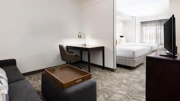 Ett hotellrum med en soffa, ett skrivbord med en lampa, en tv och en säng.