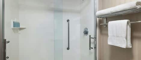 Een douche met glazen wand, een handgreep, een witte handdoekhouder en een klein plankje met toiletartikelen.