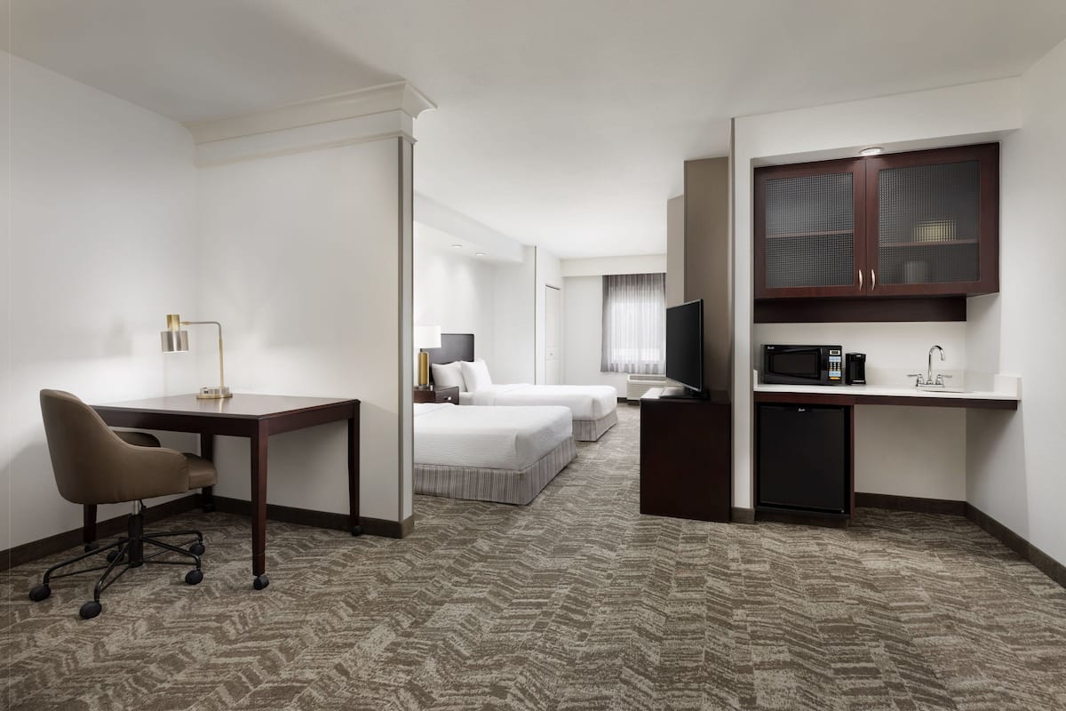 A hotel room with a desk, two beds, a TV, a microwave, and a minibar.