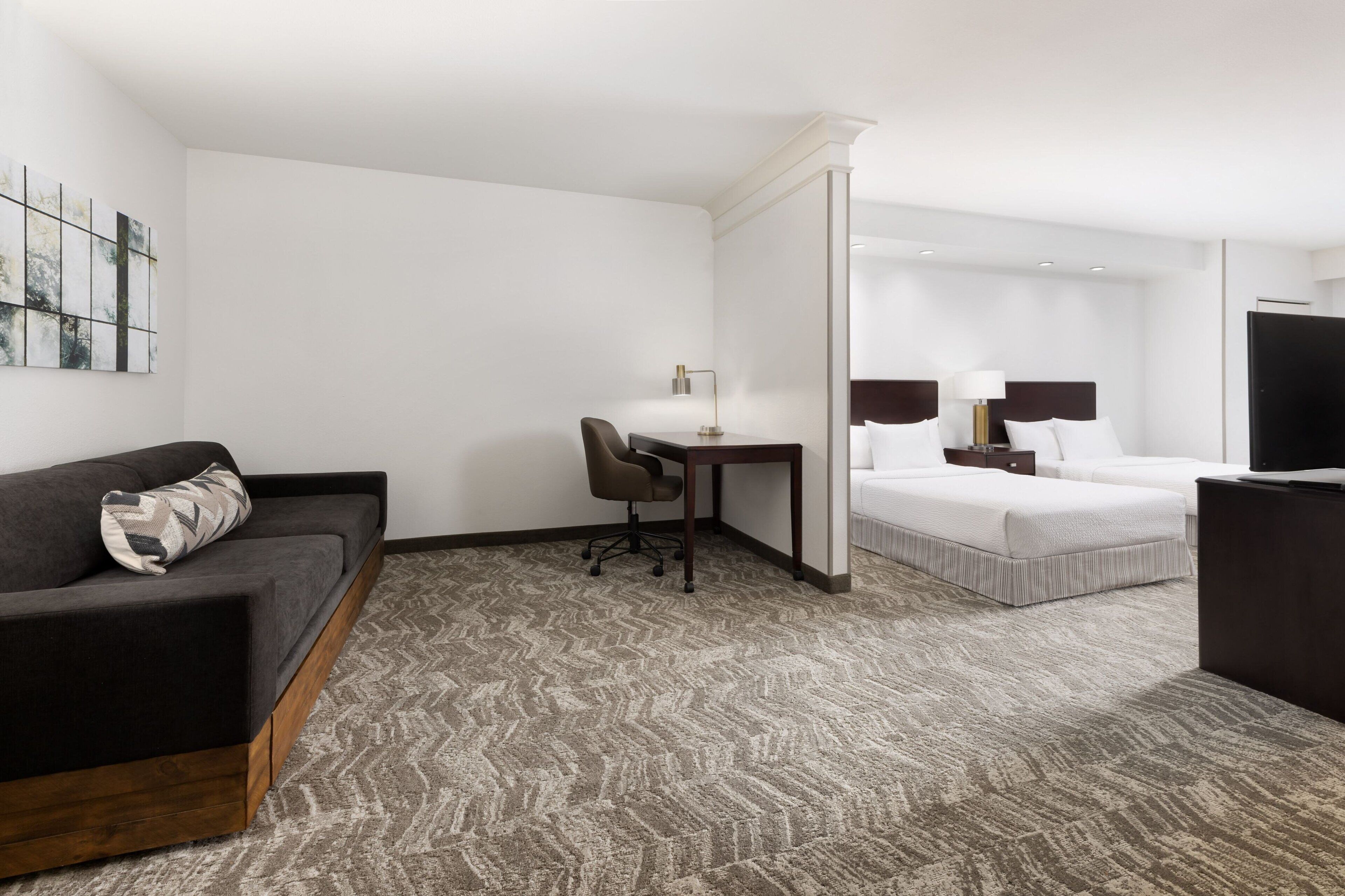 A hotel room with a sofa, a desk, a chair, a bed, and a TV.