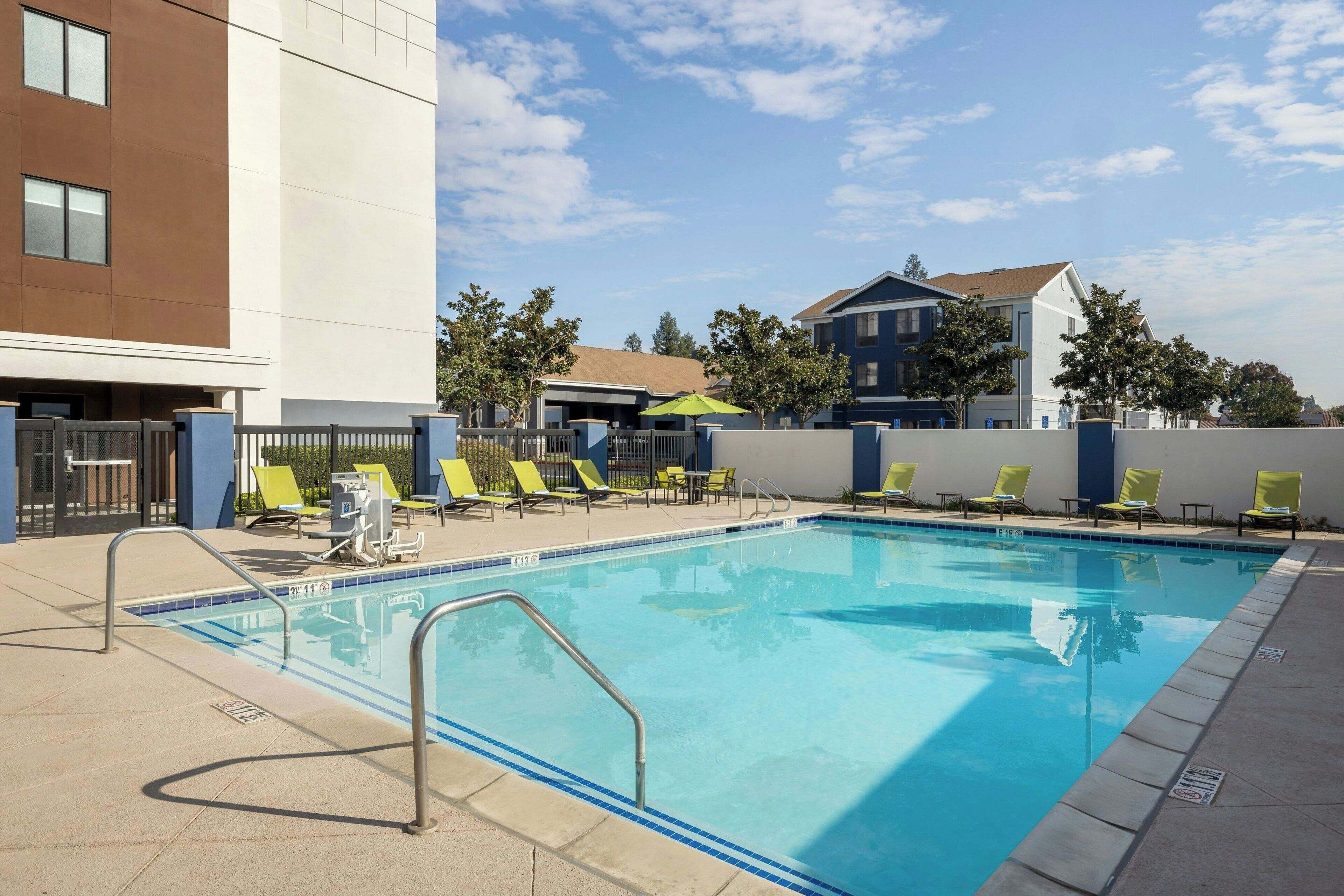 A swimming pool with lounge chairs, a fence, and a building with a brown and white facade.