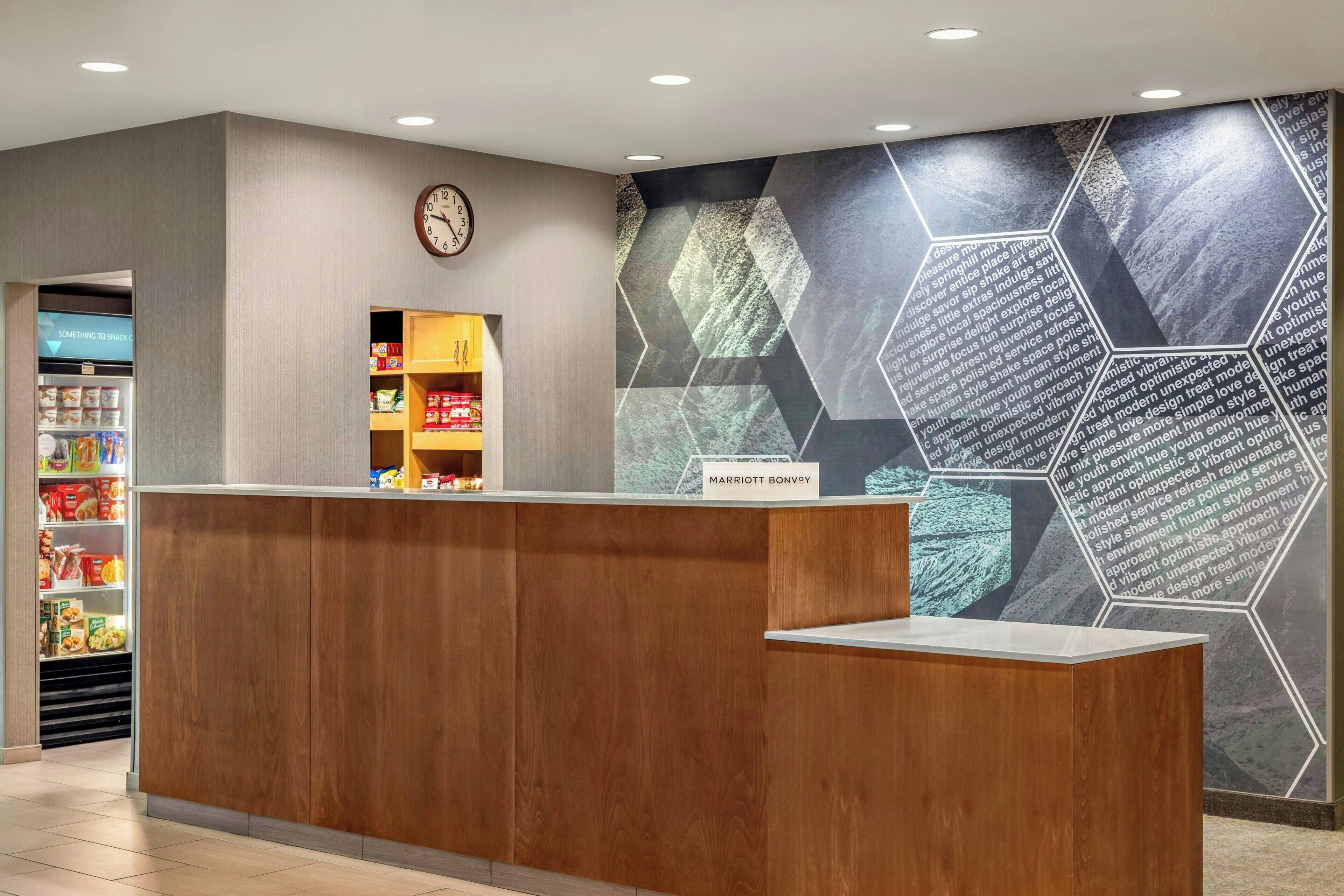 Een hotel receptiebalie met een klok, een aanrecht met een bord en een muur met geometrische patronen.