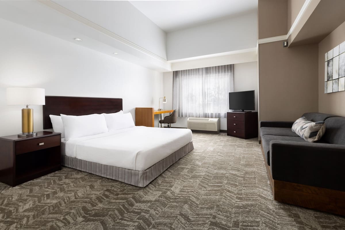 A hotel room with a large bed, a sofa, a TV, and a desk with a lamp.
