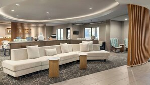 A modern lobby with a curved ceiling, a sectional sofa, round tables, and a reception desk. - SpringHill Suites by Marriott Fresno (Fresno)