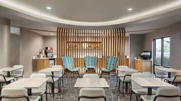 Une chambre d’hôtel moderne dotée d’un espace salon central, d’une kitchenette et d’une grande fenêtre offrant une vue dégagée.
