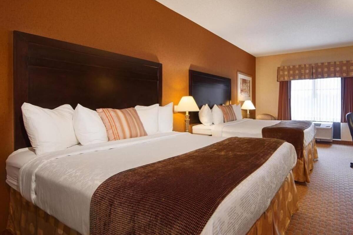 Habitación de hotel con dos camas, un cabecero grande y oscuro, un televisor de pantalla plana y una ventana con cortinas.